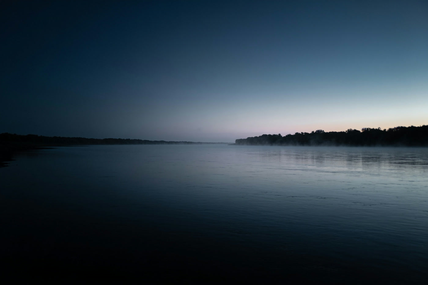 A wide river before sunrise, mist on the surface